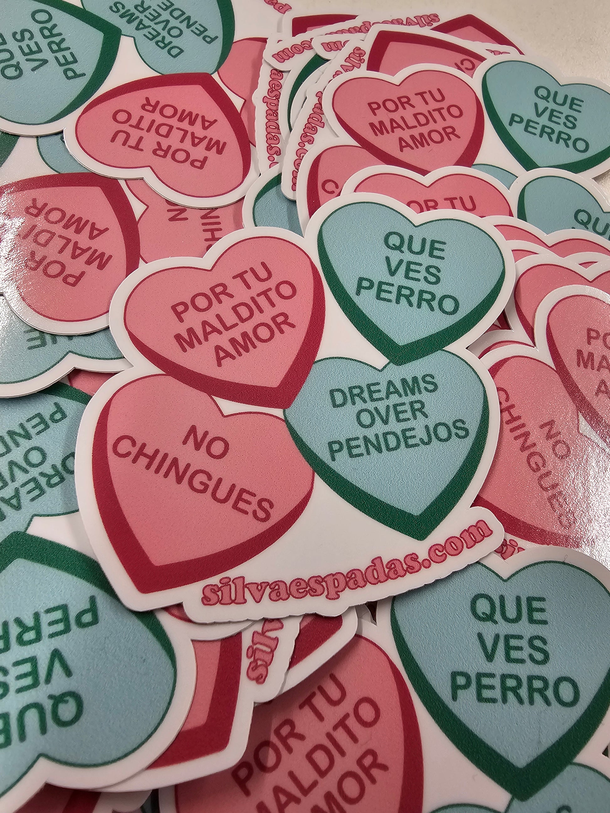 die-cut heart-shaped stickers with various messages in Spanish, such as que ves perro and dreams over pendejos