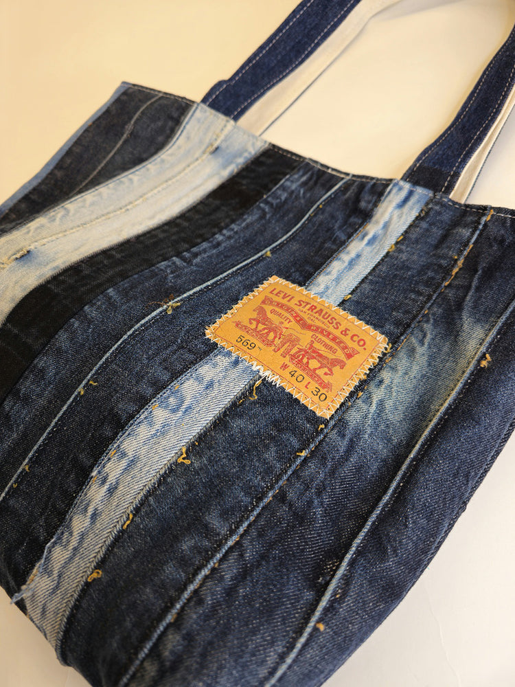 A blue denim patchwork tote bag, featuring distressed details and a brand tag on the lower side.