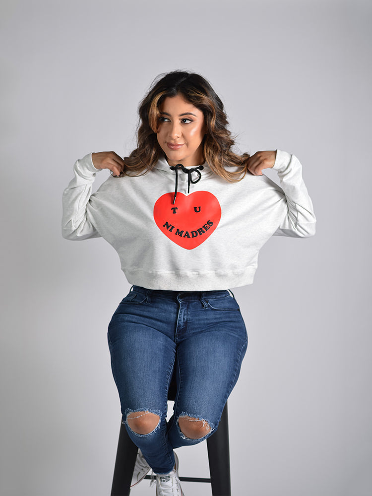 Latina modeling a gray cropped hoodie with a red heart and text "Tu ni madres" screen printed on the front