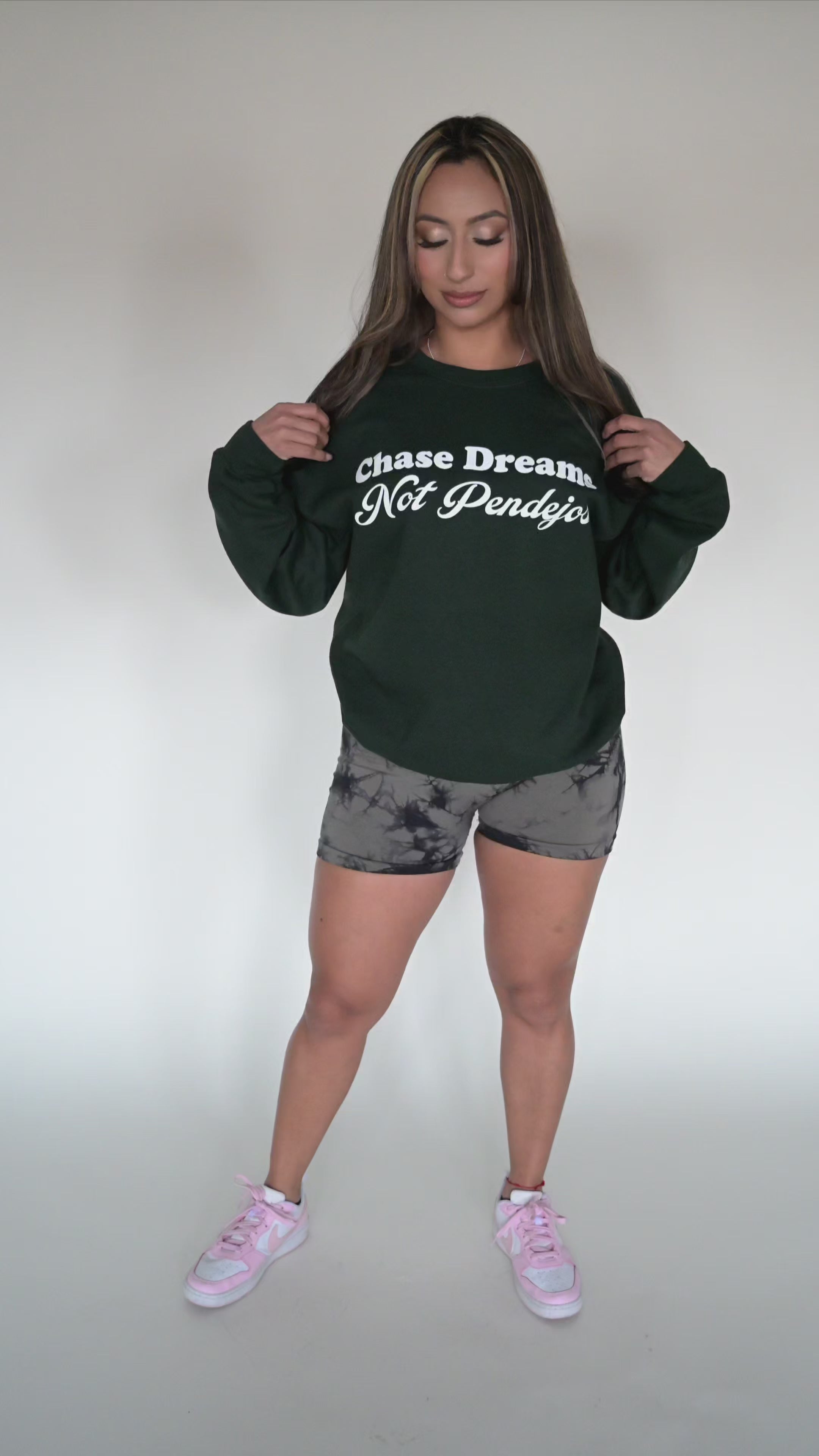 Person modeling green sweater with the phrase " Chase Dreams Not Pendejos" screen printed on the front