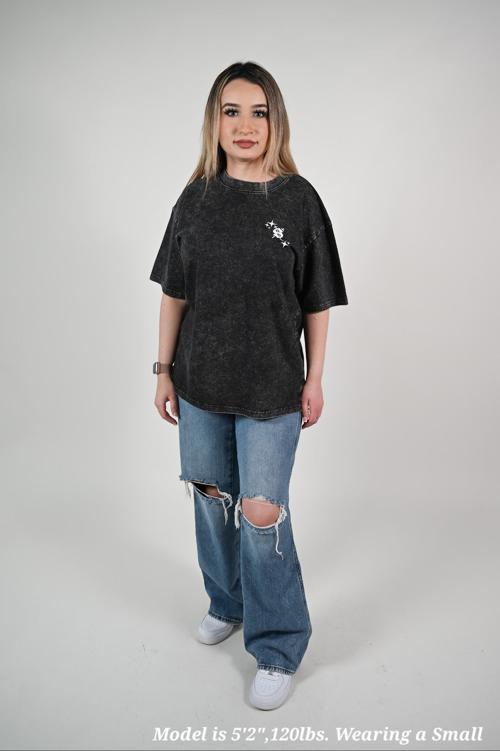 Latina model wearing an oversized black t-shirt and ripped jeans on a plain background