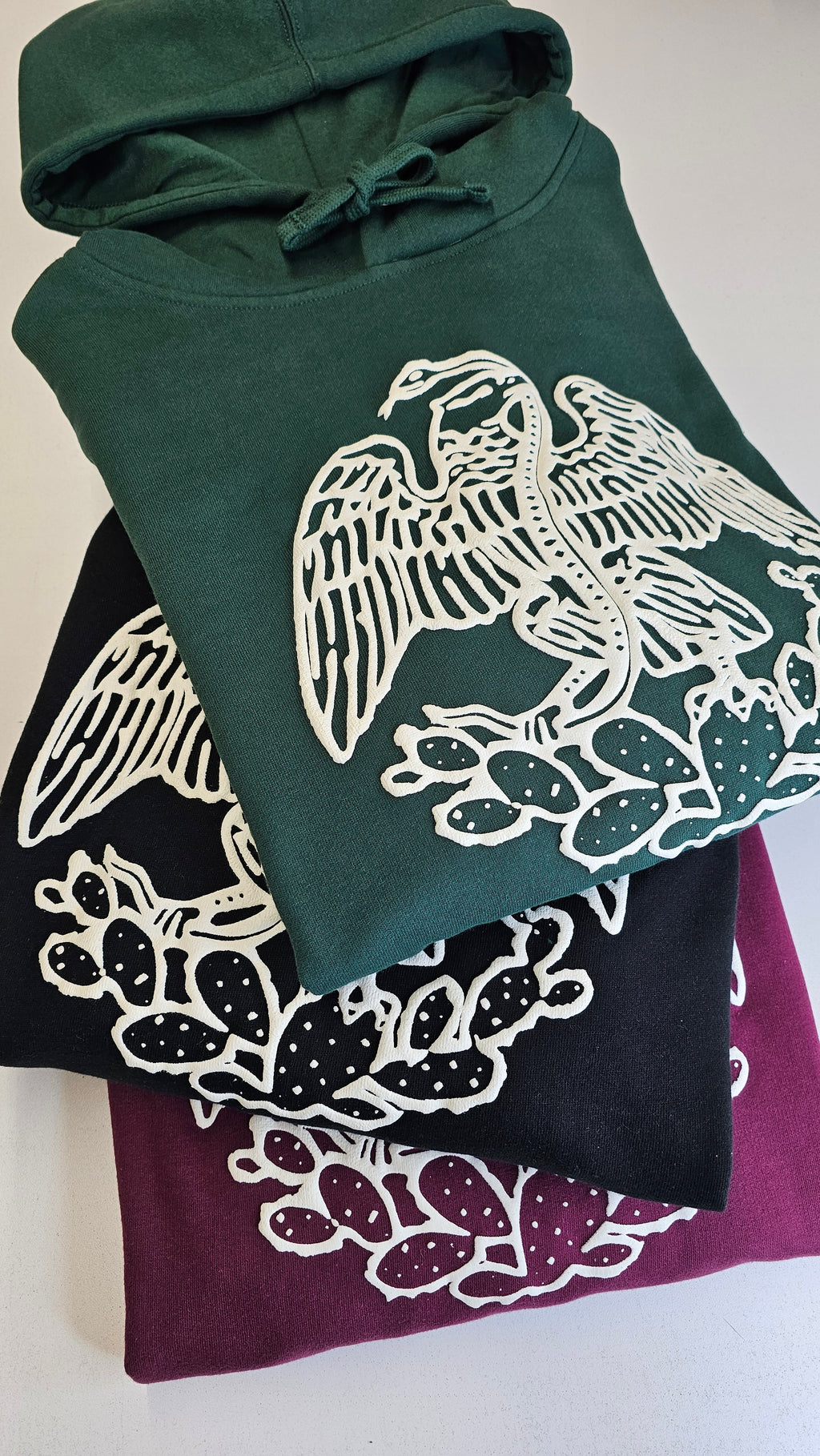 Three hoodies with white floral patterns on green, black, and purple backgrounds.