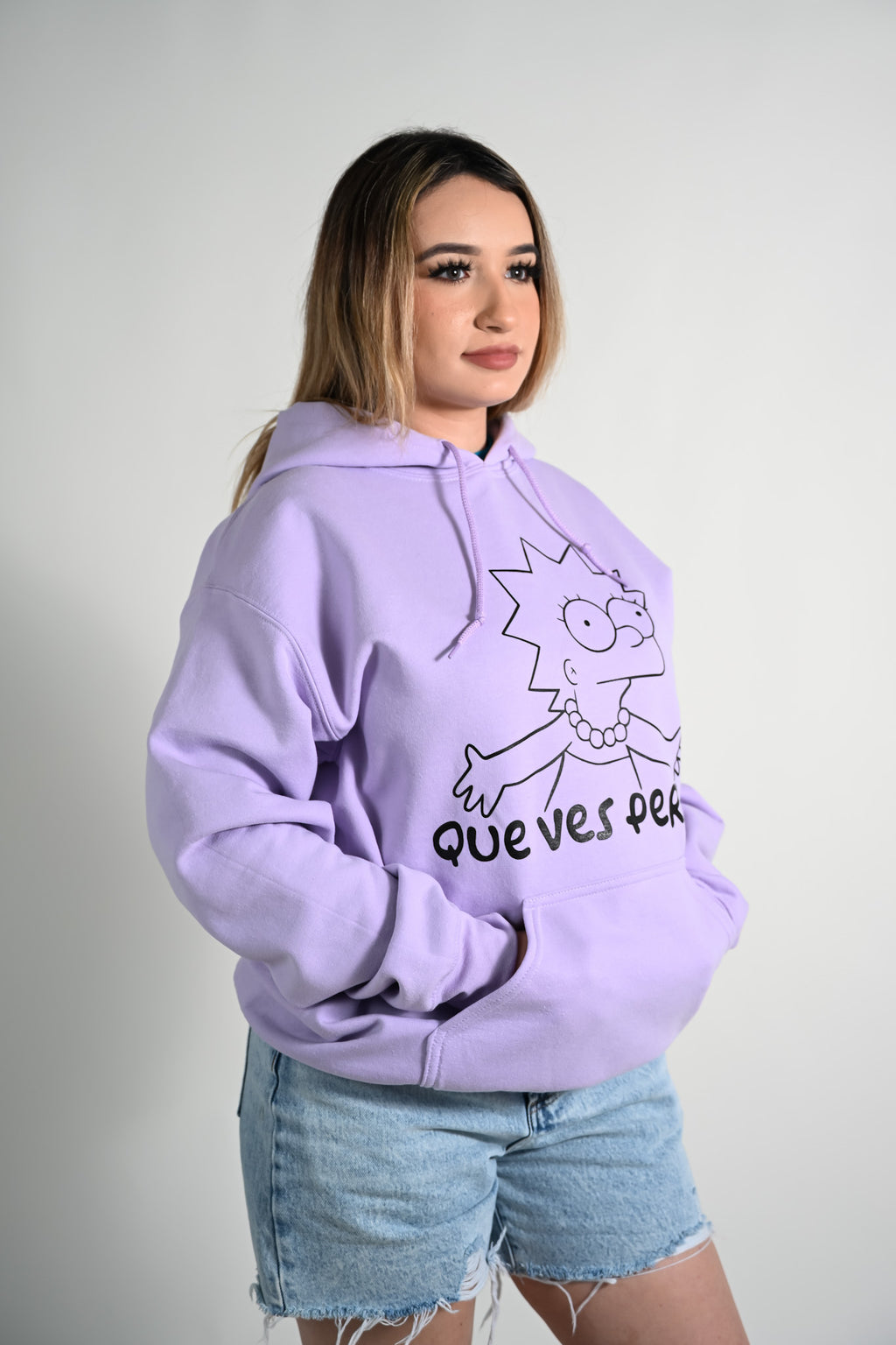 Latina wearing a light purple hoodie with a graphic design and text on a plain background