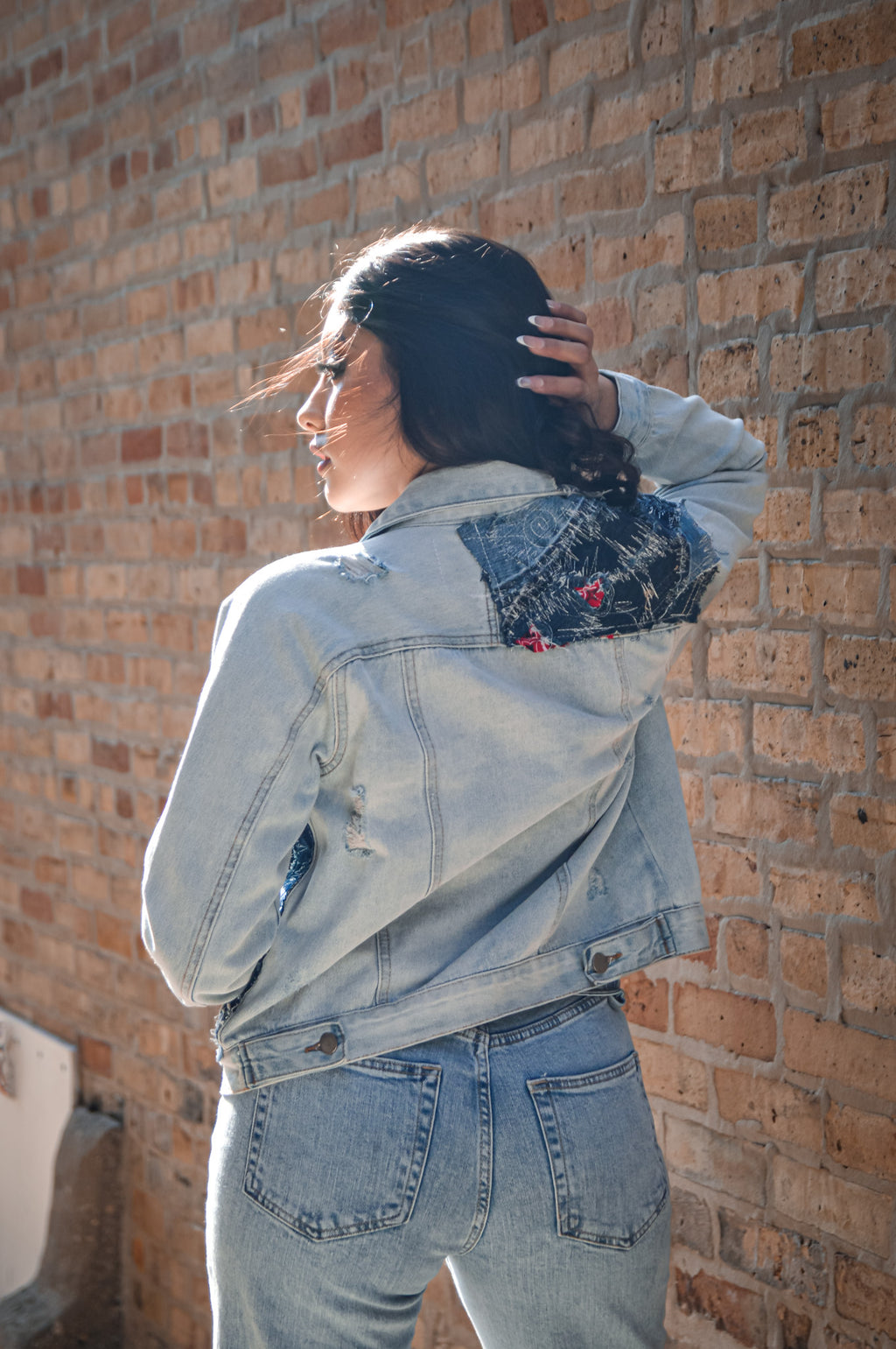 Rear view of cropped denim patchwork jacket with visible seamwork and sleeve paneling in light and dark washes
