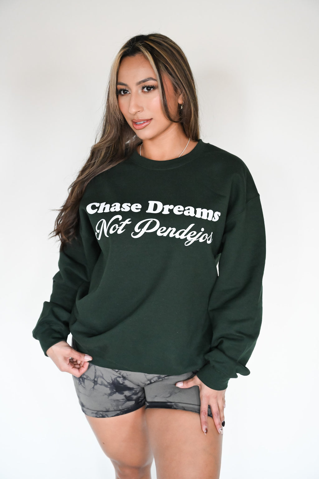 Person wearing a green sweater with white text "Chase dreams not pendejos"