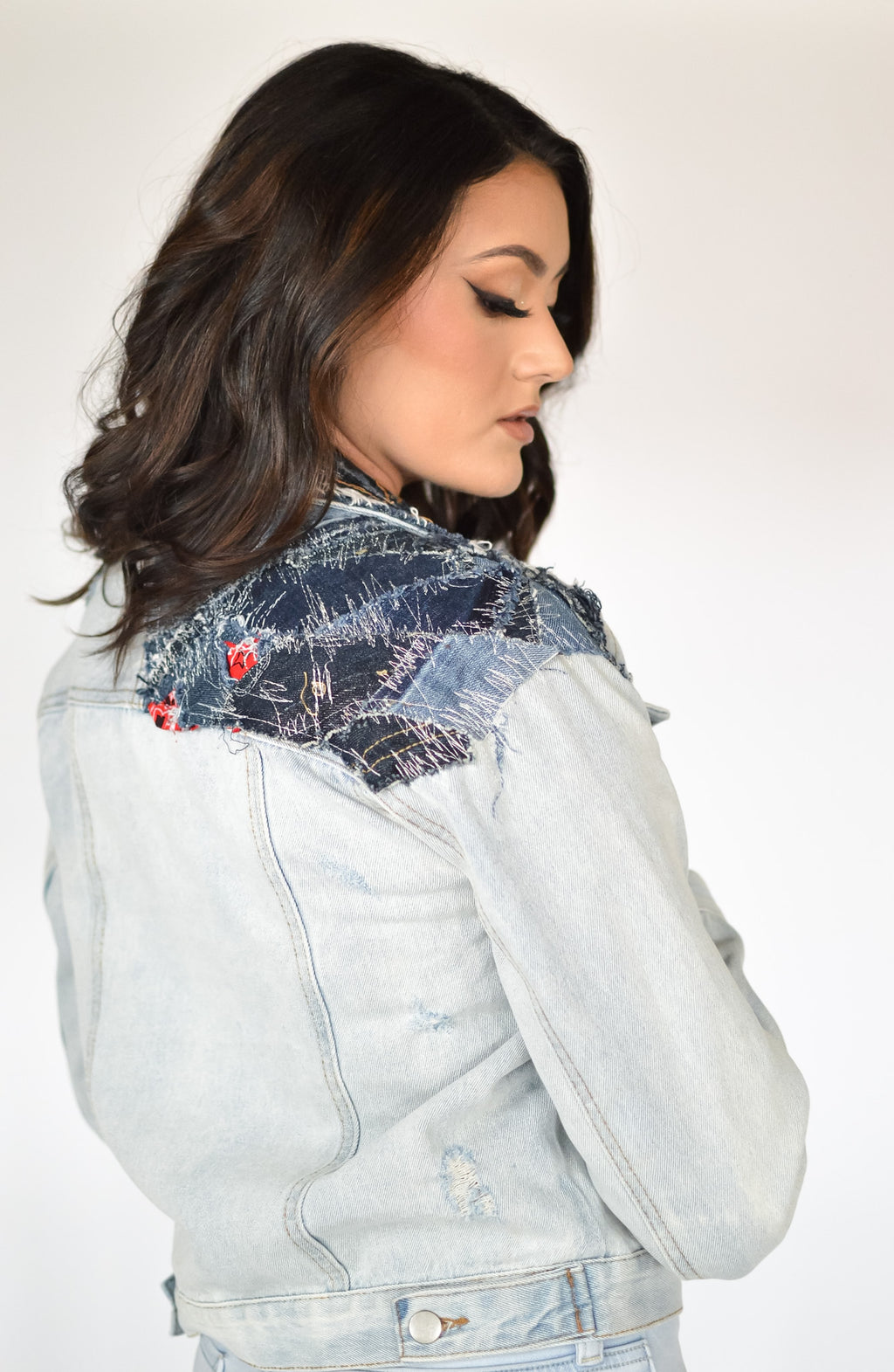 Rear view of cropped denim patchwork jacket with visible seamwork and sleeve paneling in light and dark washes