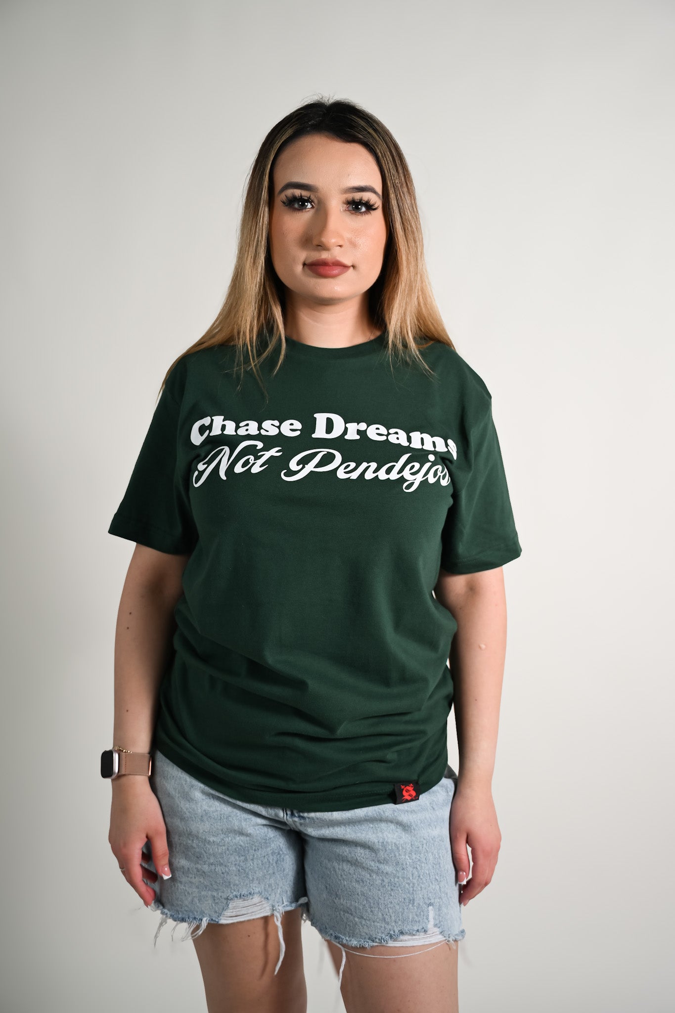 Person wearing a green t-shirt with text Chase dreams not pendejos, standing against a plain background