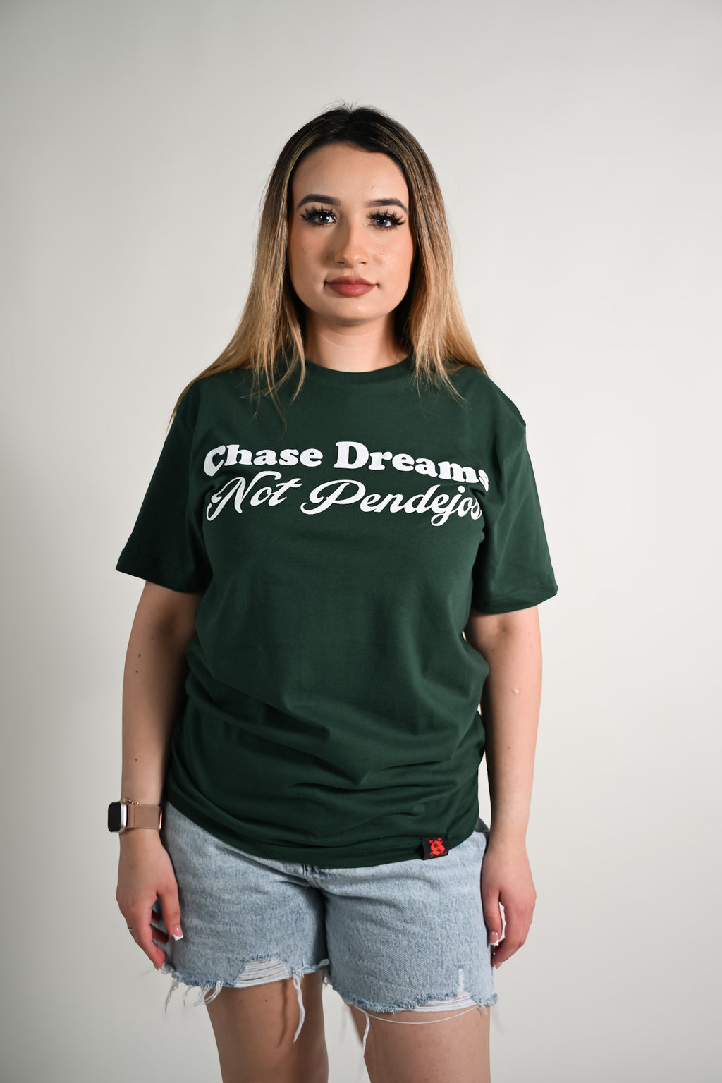 Person wearing a green t-shirt with text Chase dreams not pendejos, standing against a plain background