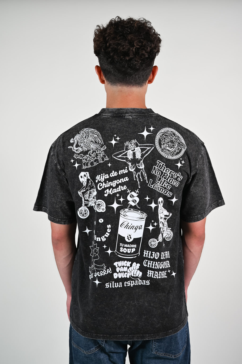 Model wearing black acid-wash oversized t-shirt with bold Latino-inspired white graphics and cultural phrases on the back, including 'Hija de mi Chingona Madre' and 'Chinga Tu Madre Soup' by Silva Espadas