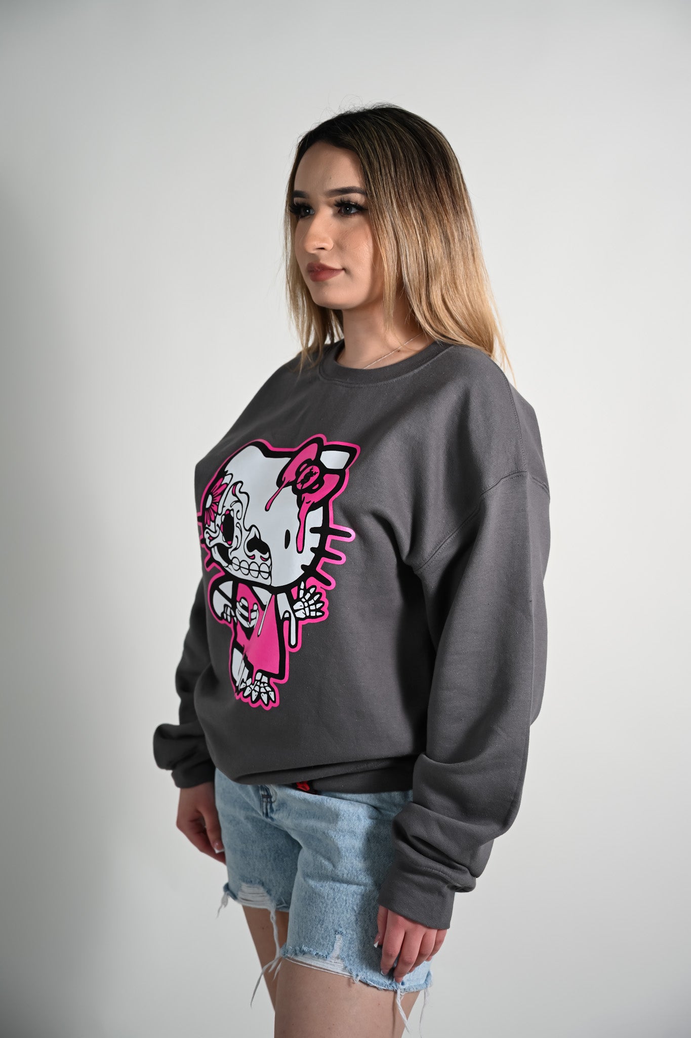 Woman wearing a gray sweatshirt with a colorful hello kitty skeleton graphic design on a plain background