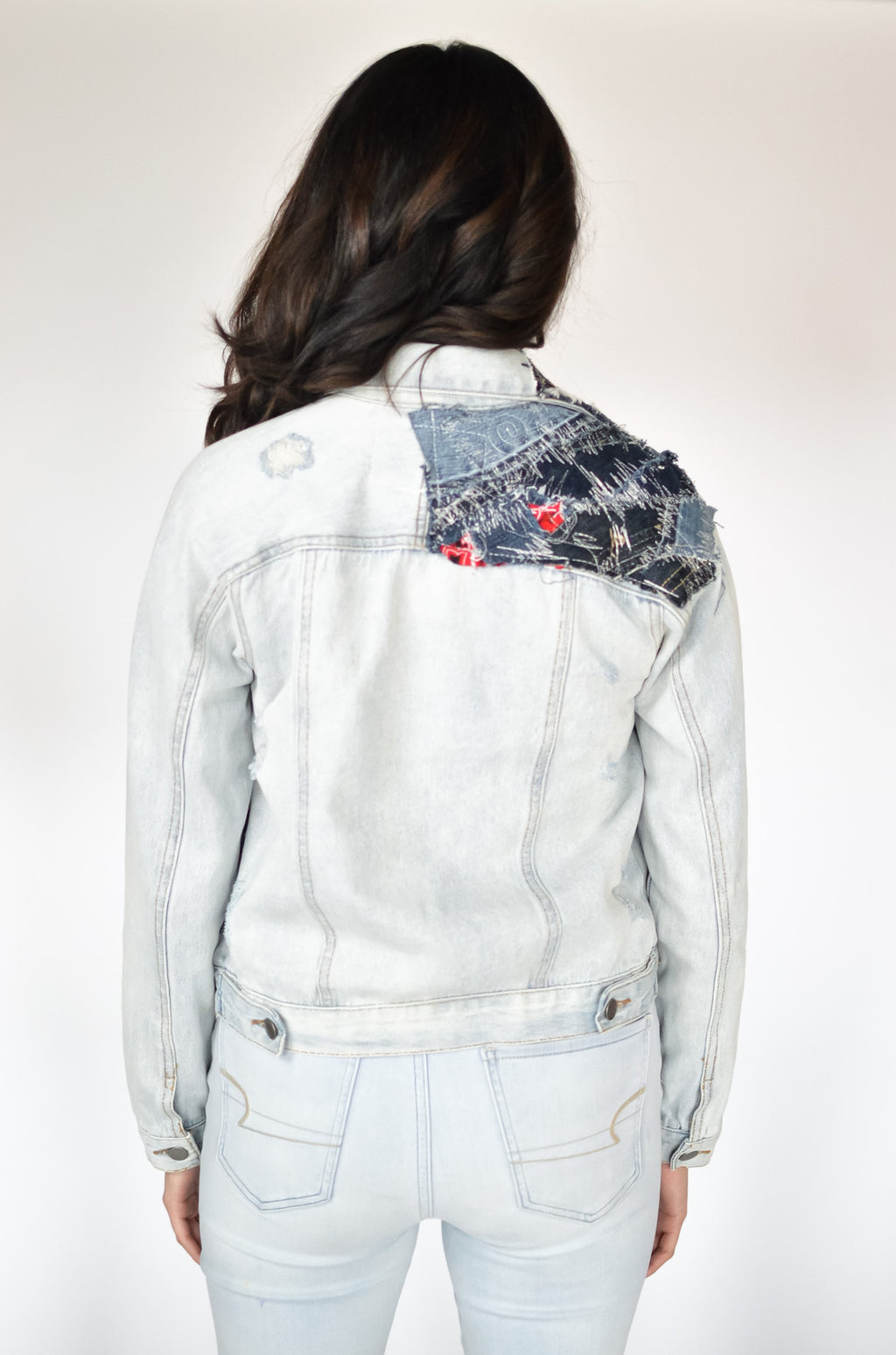 Rear view of cropped denim patchwork jacket with visible seamwork and sleeve paneling in light and dark washes