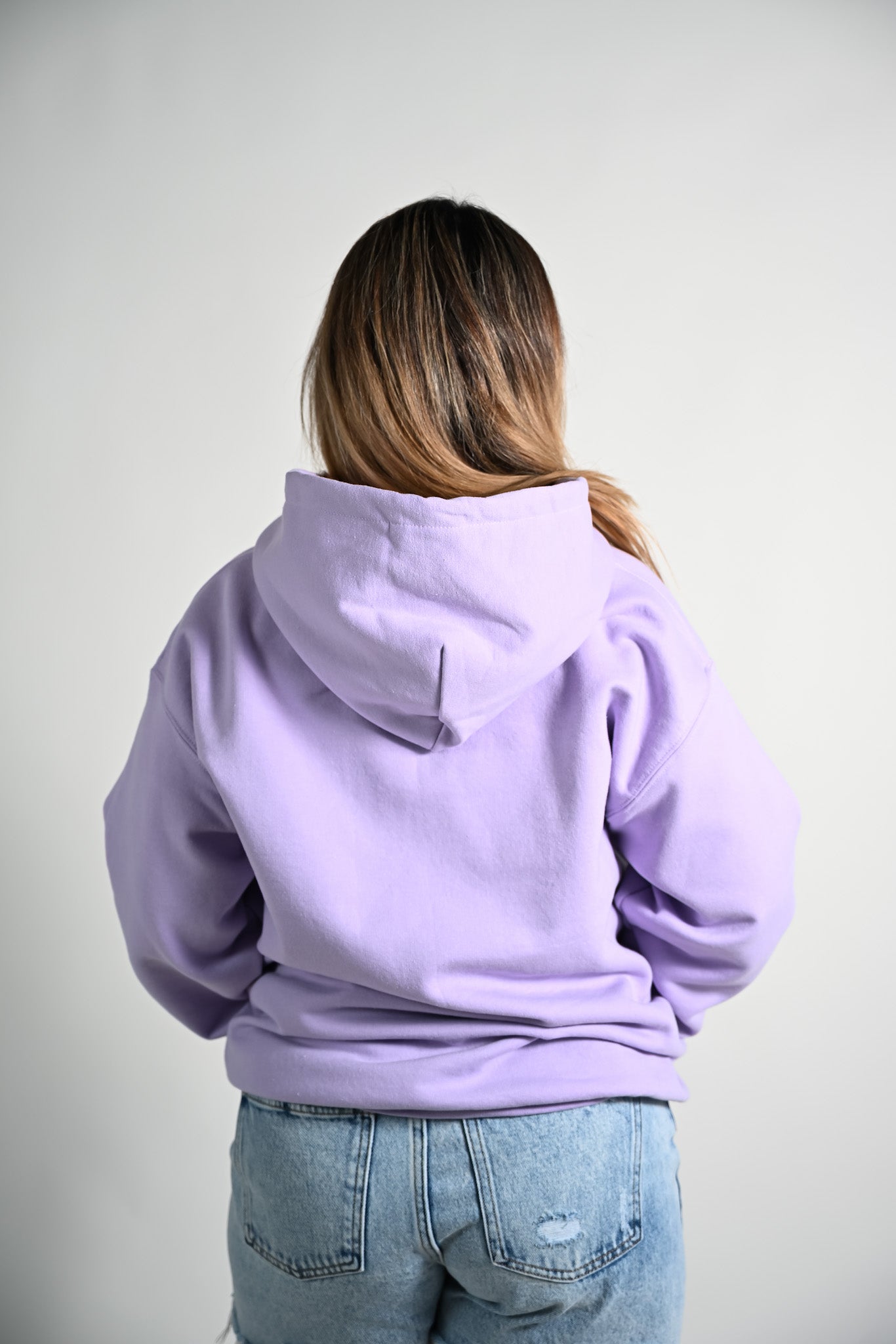 Person wearing a light purple hoodie and blue jeans on a plain background