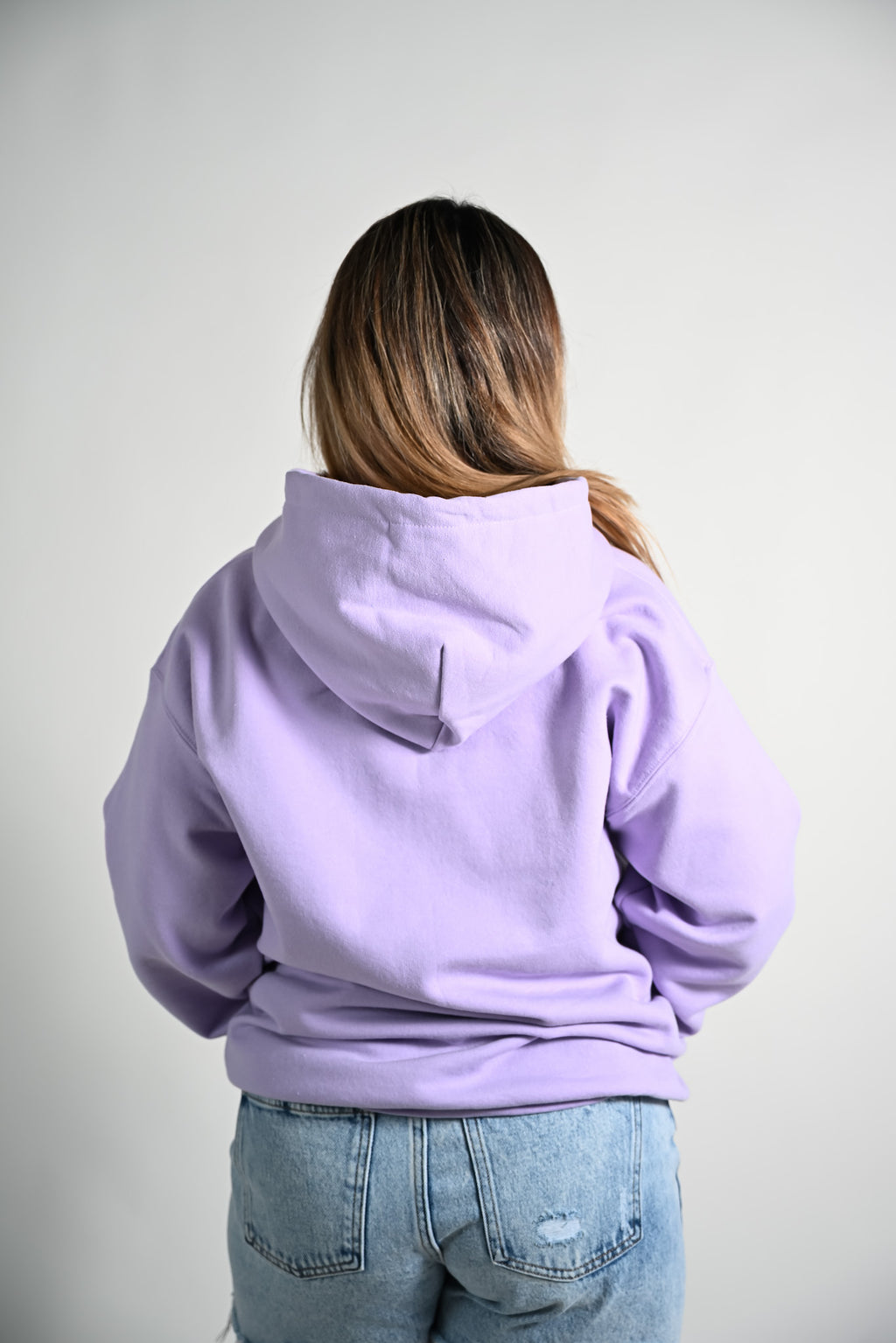 Person wearing a light purple hoodie and blue jeans on a plain background