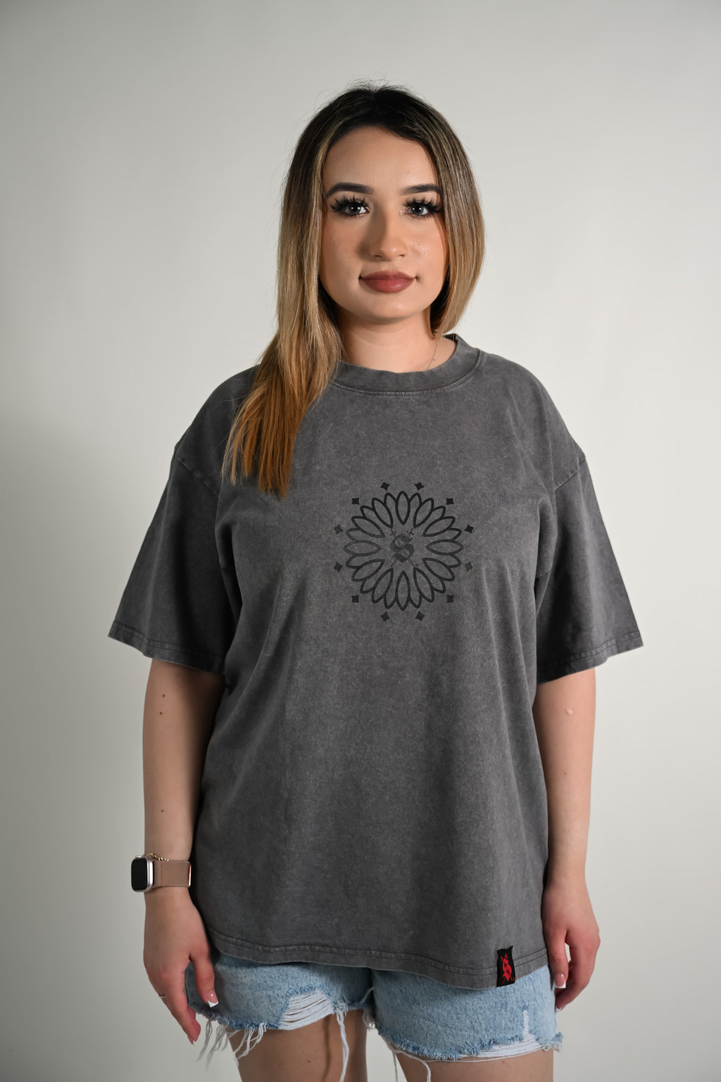 Woman wearing a gray t-shirt with a black mandala design on a plain background