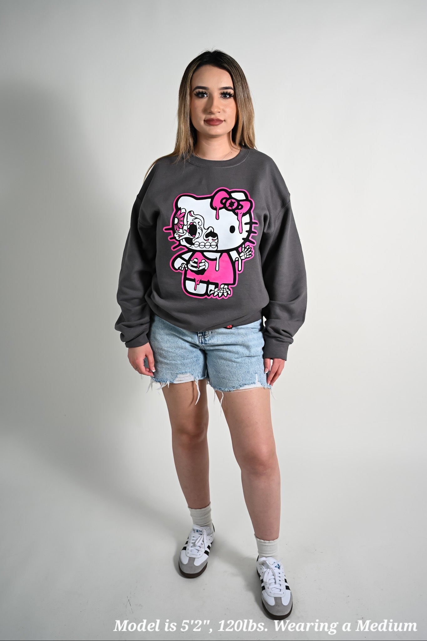 Person wearing a gray sweatshirt with a Hello Kitty design dia de los muertos on a plain background