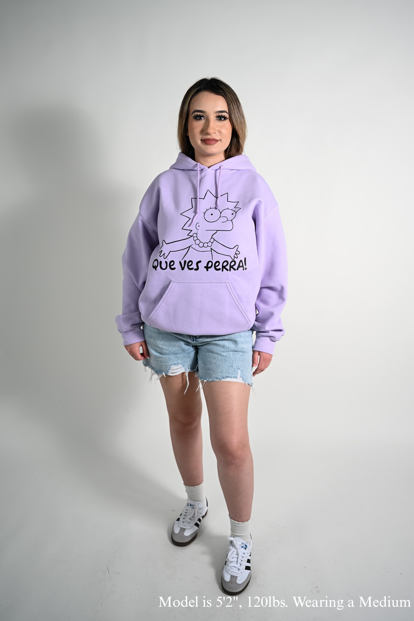 Person wearing a light purple hoodie with que ves perra text and Lisa graphic on a plain background
