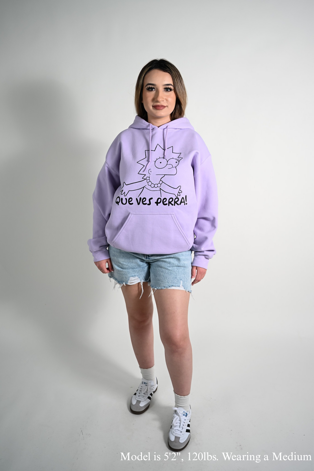 Person wearing a light purple hoodie with que ves perra text and Lisa graphic on a plain background