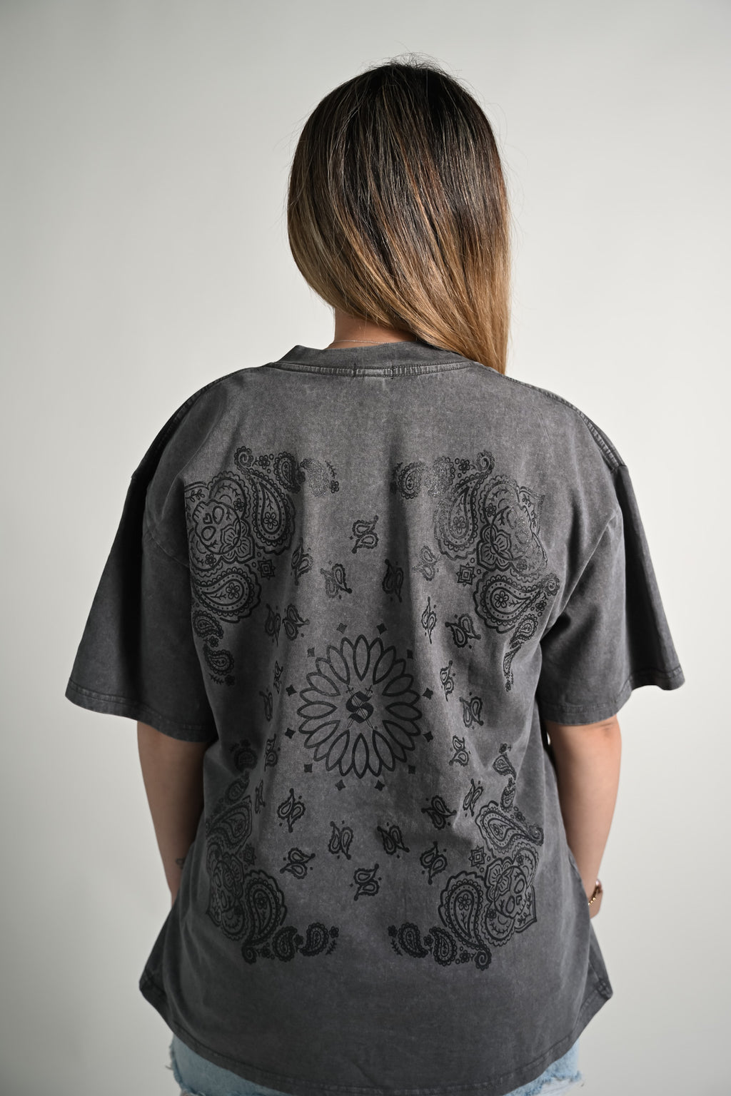 Person wearing a gray oversized t-shirt with paisley bandana patterns on the back against a plain background