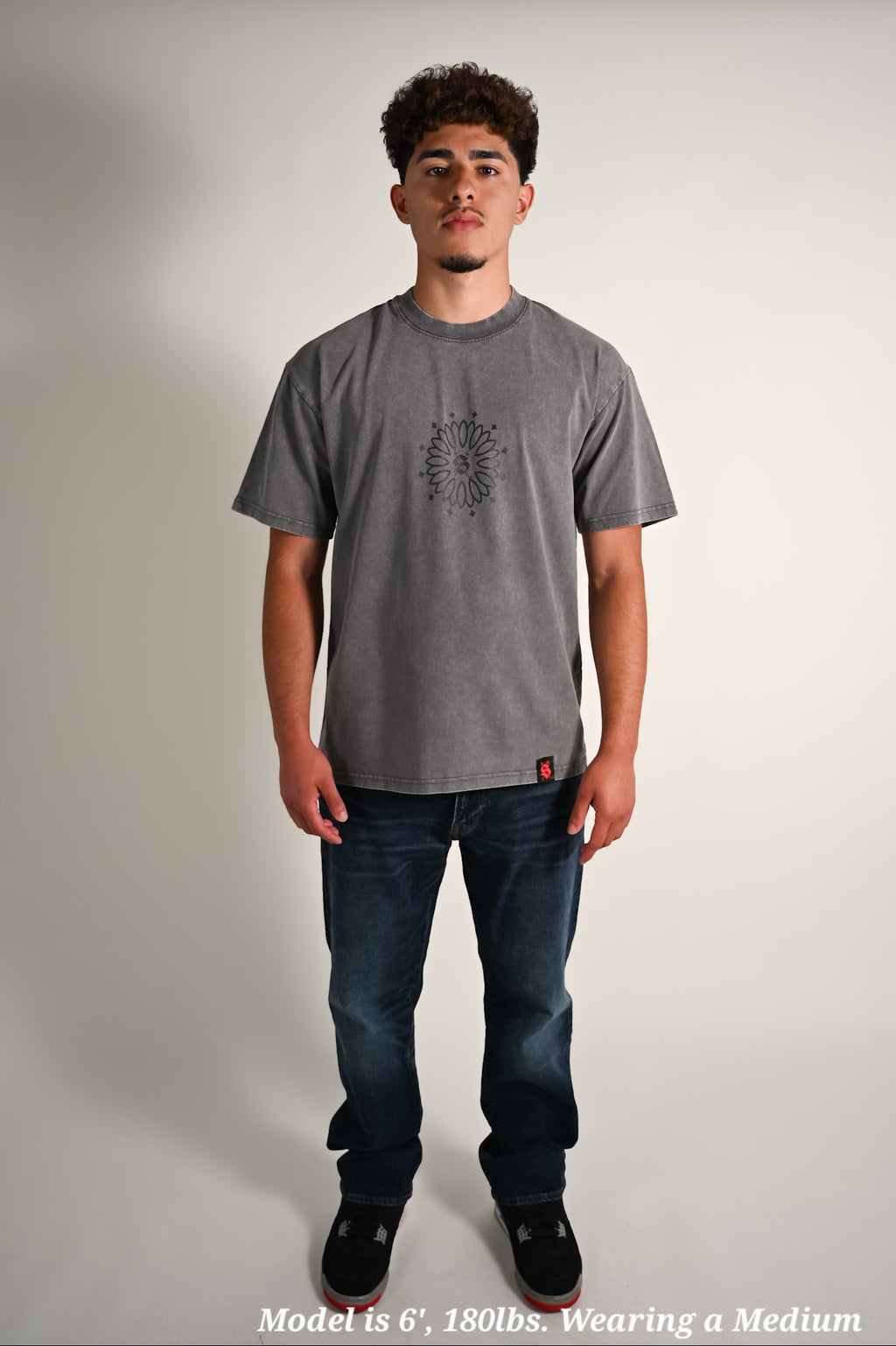 Latino wearing a gray oversized t-shirt with a logo and dark jeans on a plain background