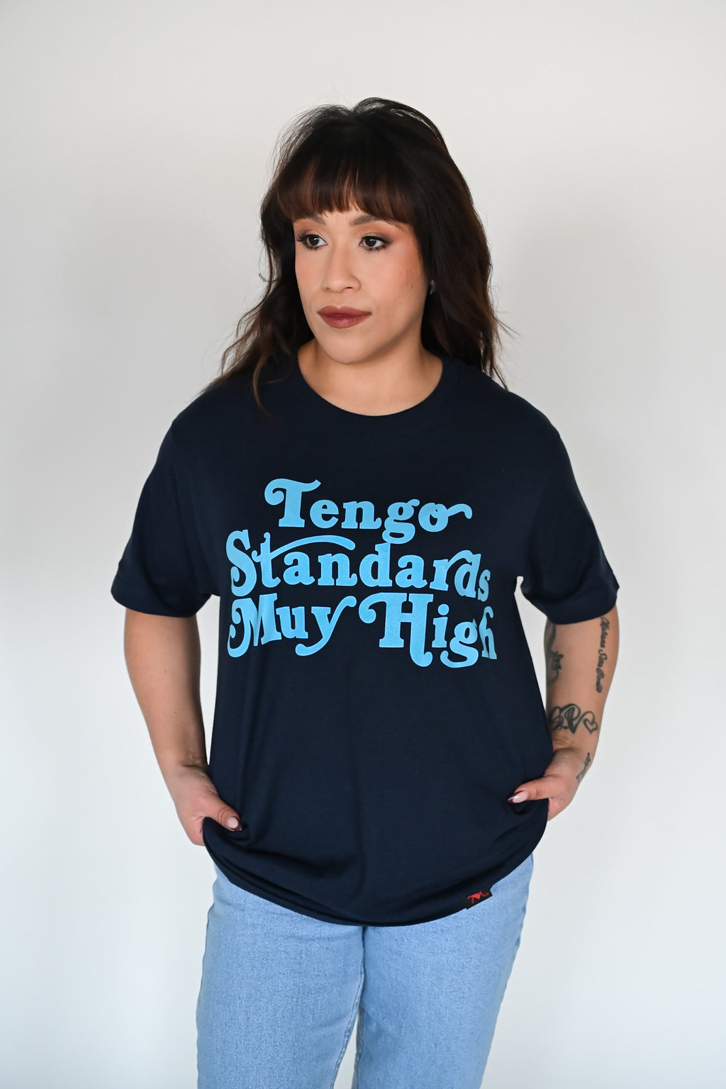Person wearing a navy blue shirt with teh text "Tengo standards muy high" printed on the front