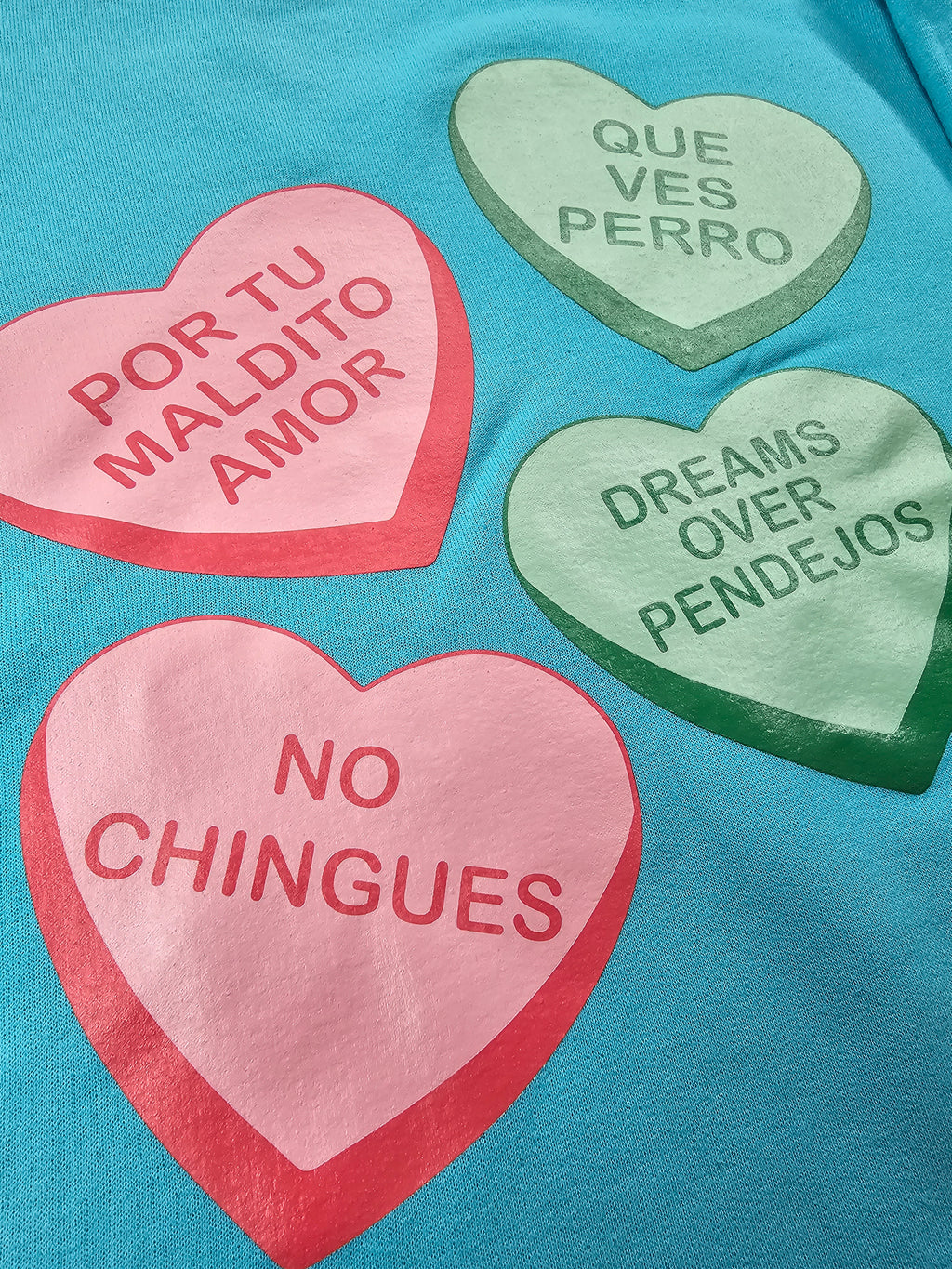 Close up of Maldito Amor graphic design on blue sweater by Silva Espadas