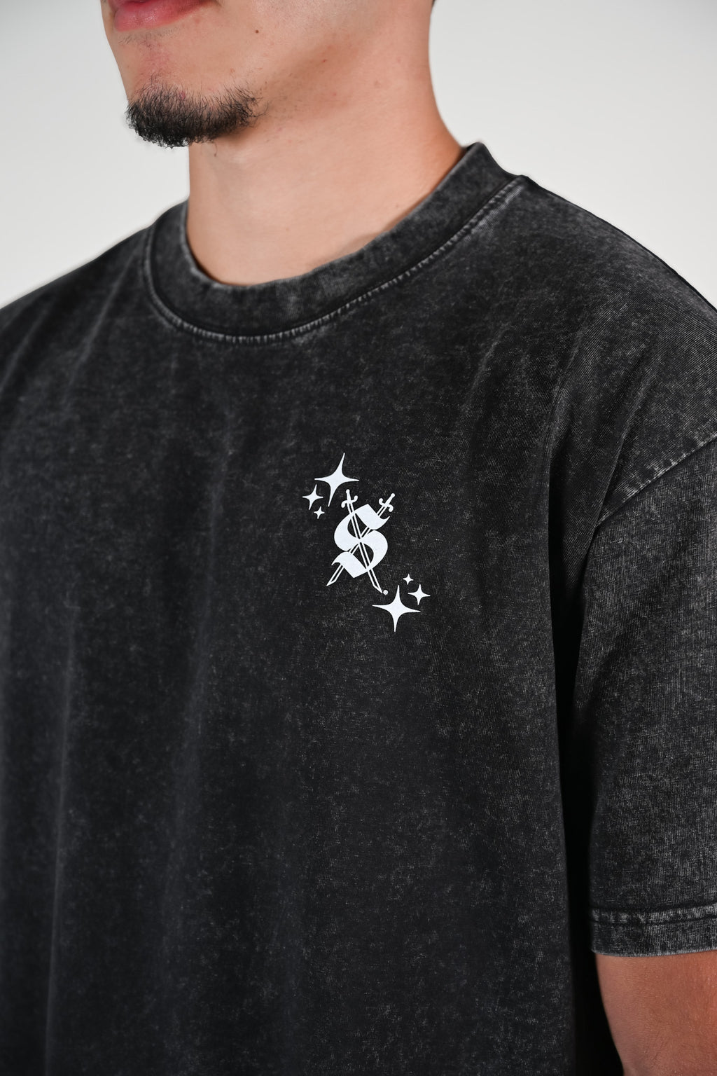 Close up of black acid-wash oversized tee with Silva Espadas swords and S logo on left chest and white sparkle accents
