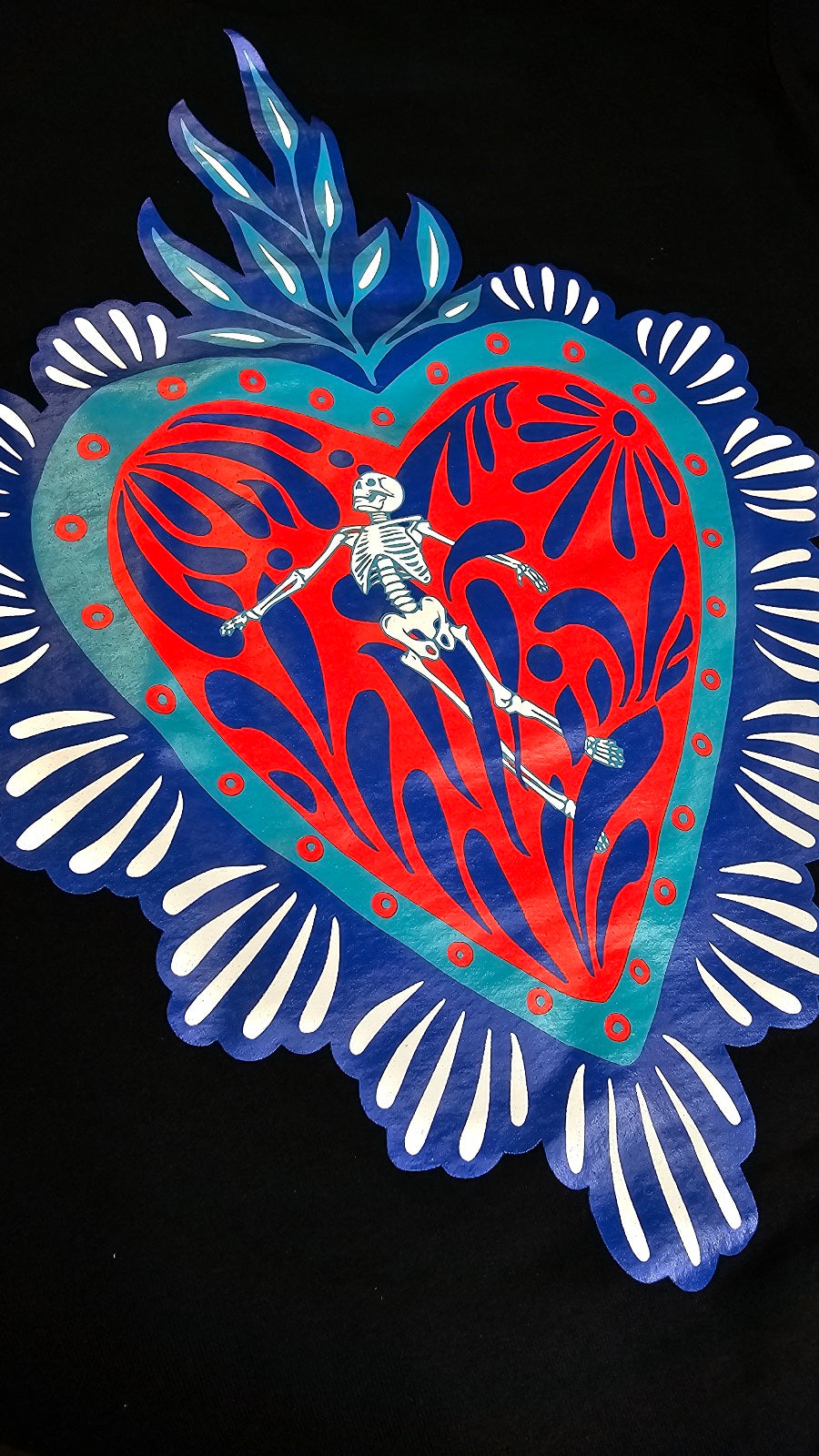 Detail shot of a talavera heart with skeleton on a black sweaterby Silva Espadas