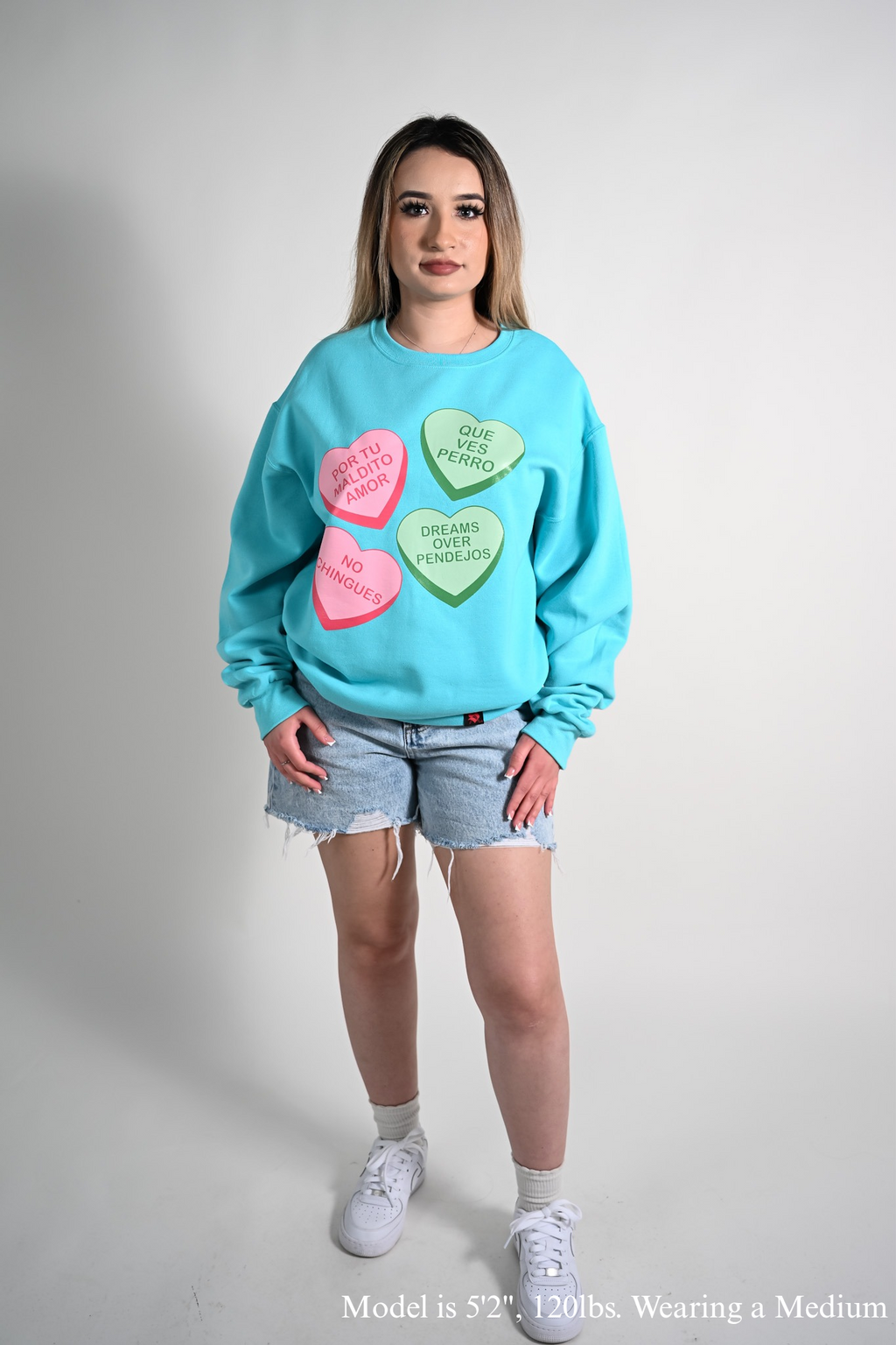 Person wearing a light blue sweatshirt with colorful Maldito Amor by Silva Espadas heart designs on a plain background