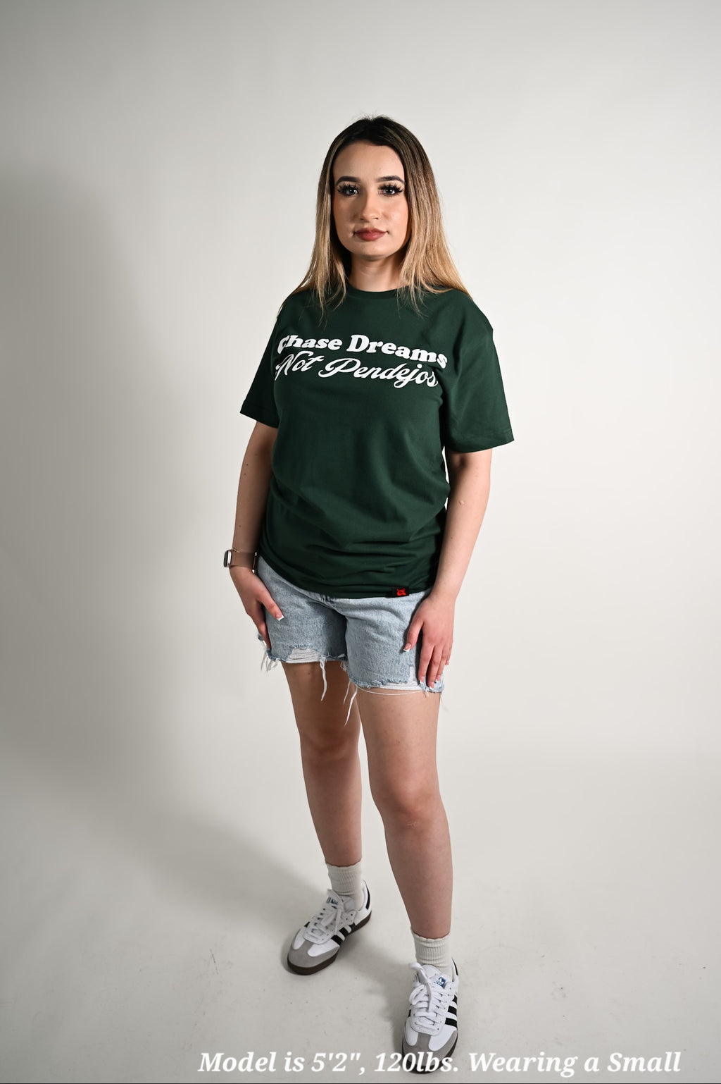 Person wearing a green t-shirt with text Chase dreams not Pandejos denim shorts on a plain background