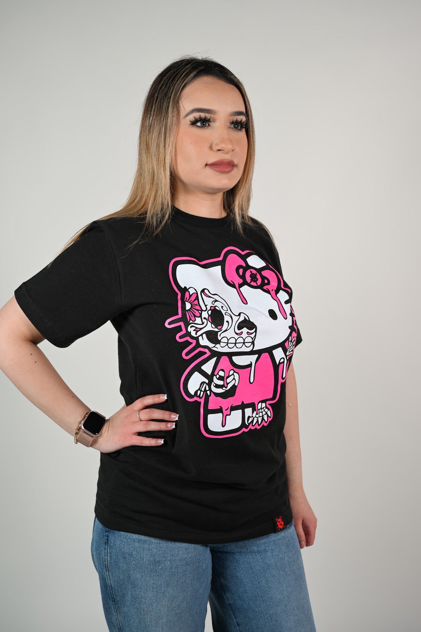 Person wearing a black t-shirt with a hello kitty skull graphic design on a plain background