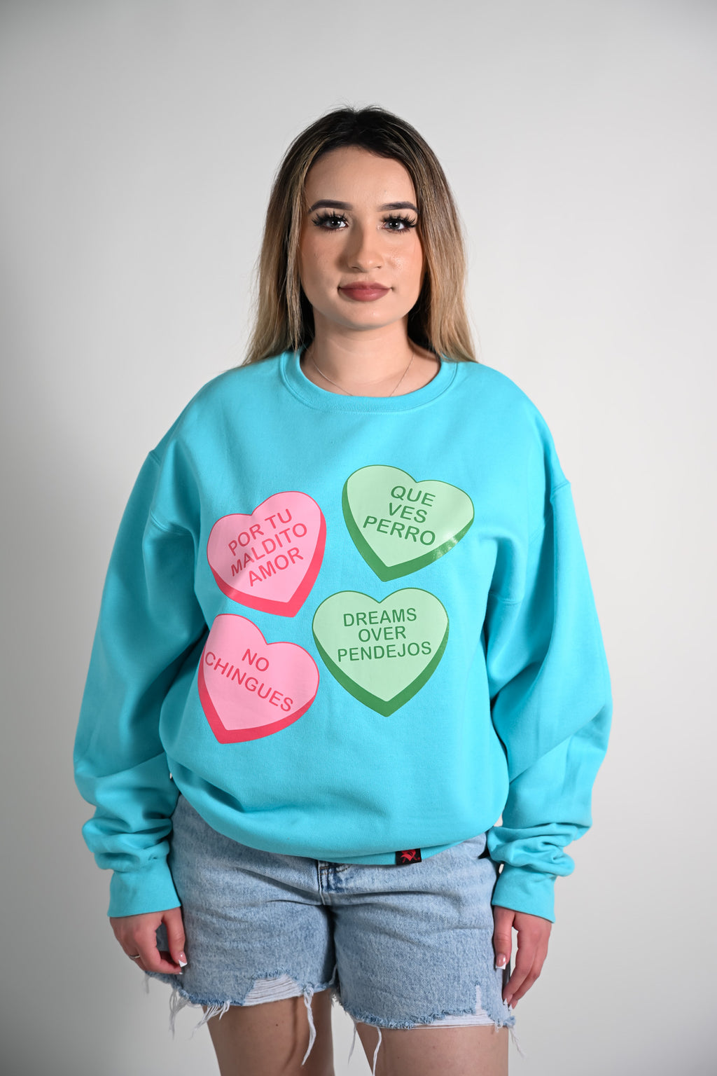 Latina wearing a light blue sweatshirt with colorful candy heart-shaped text design on a plain background