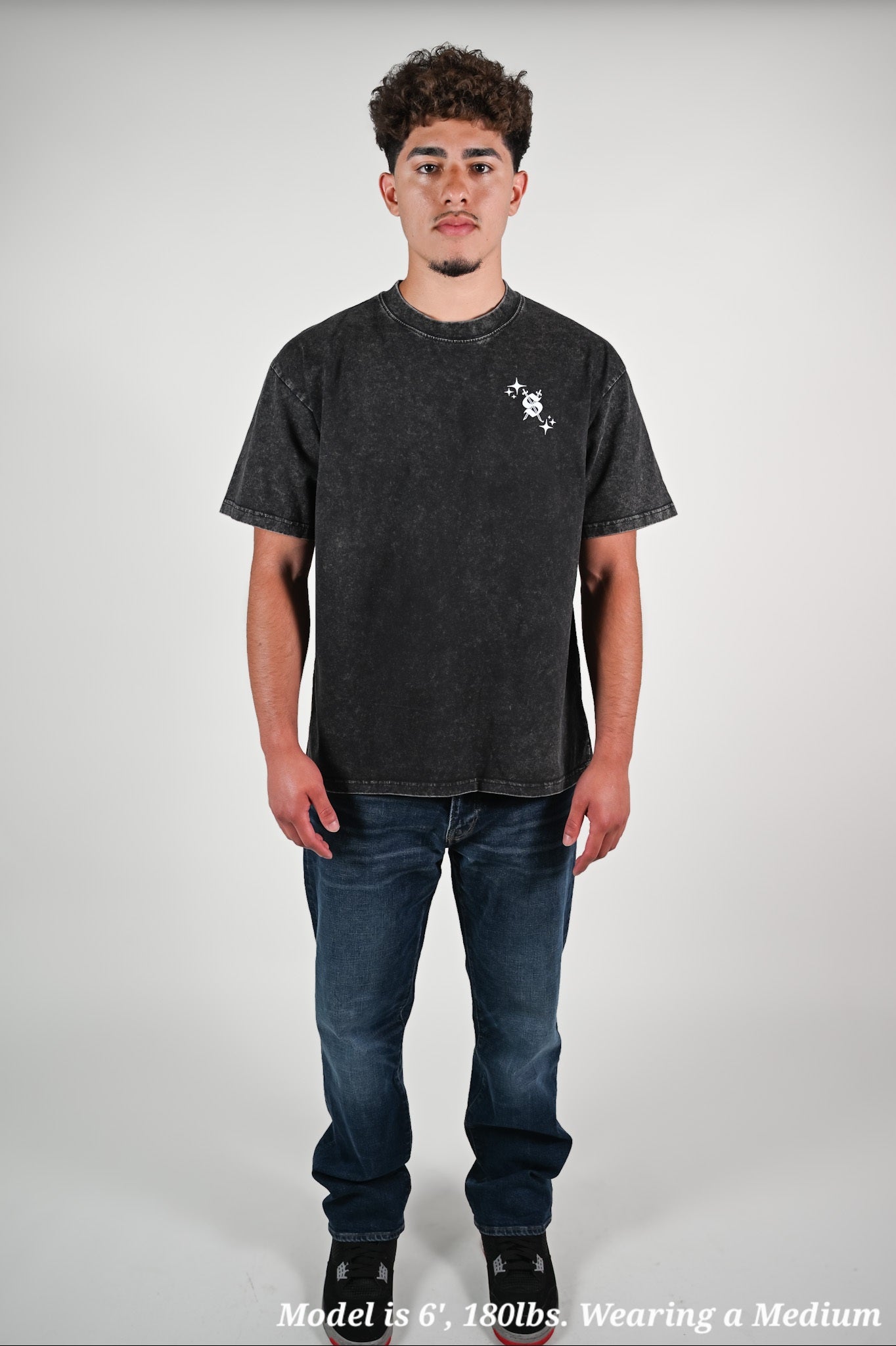 Latino model wearing a black t-shirt and jeans on a plain background