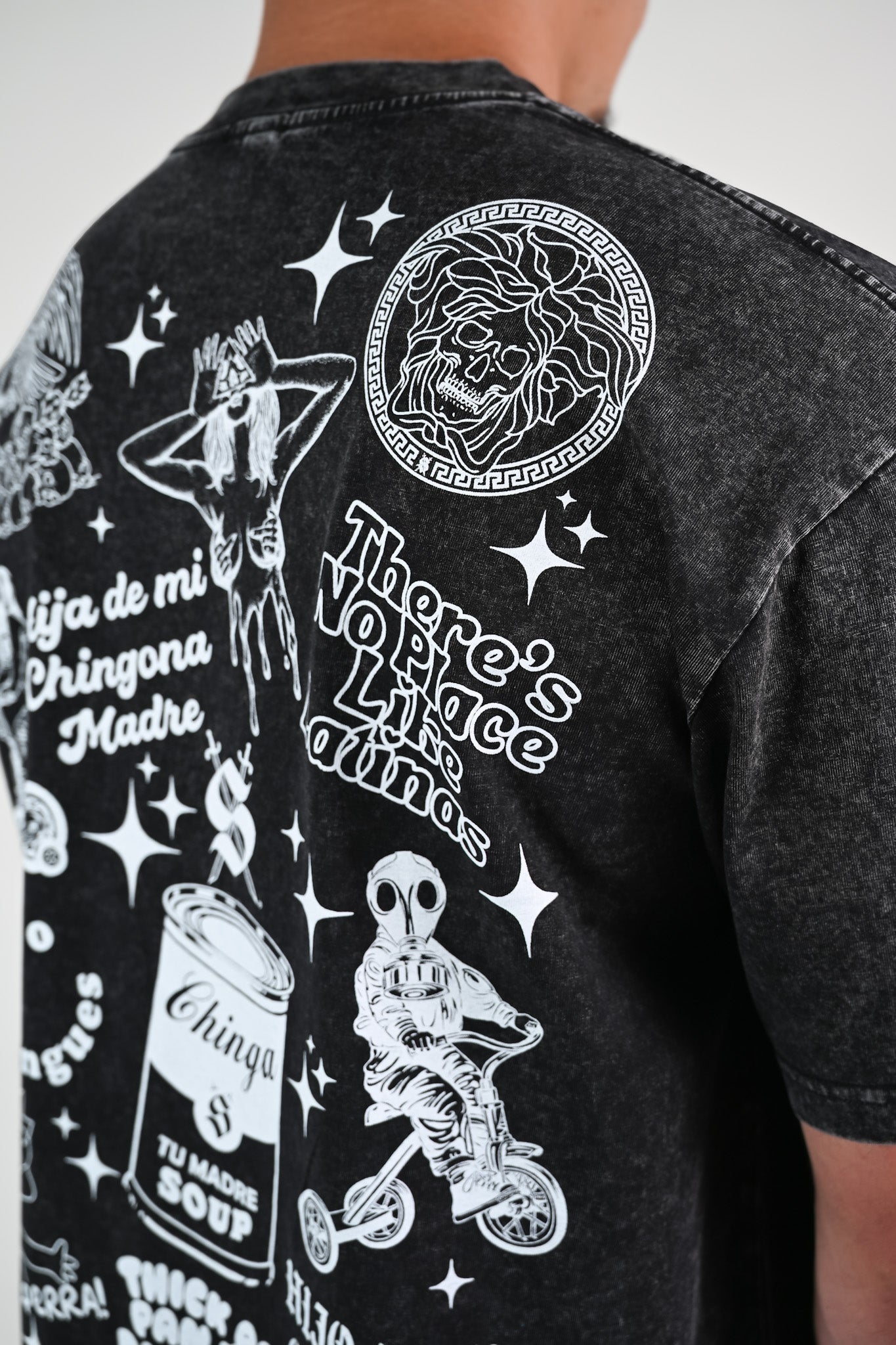 Black t-shirt with white graphic Latino-inspired designs and text like Versace skull and "there's no place like latinas"  on a plain background