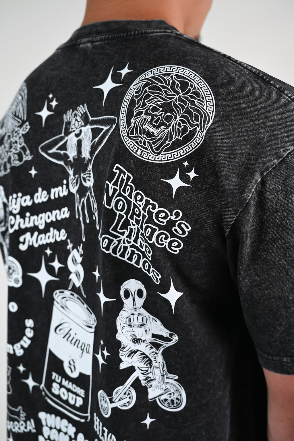 Black t-shirt with white graphic Latino-inspired designs and text like Versace skull and "there's no place like latinas"  on a plain background